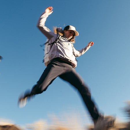 Mid leap while on a hike, wearing the Women's Dynama Pant