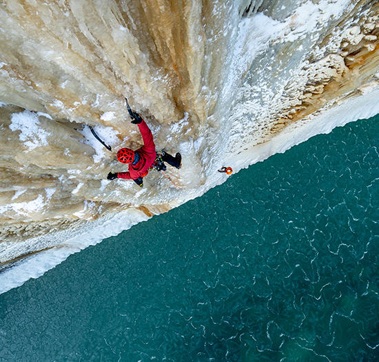 Bird eye view of an ice climber on a route above an icy ocean.