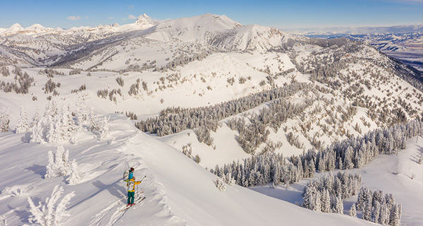 Two skiers overlook the beautiful snow-covered backcountry before skiing down a line.