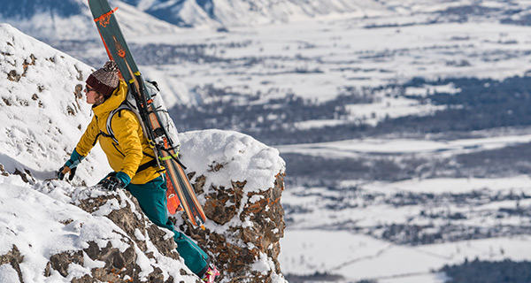 Skier climbing up some rocks in the backcountry, with skis secured on Mountain Hardwear backpack.