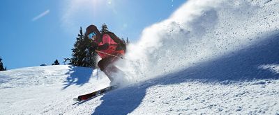 A skier wearing a pink Columbia Sportswear jacket rips down the mountain on a beautiful sunny day. 