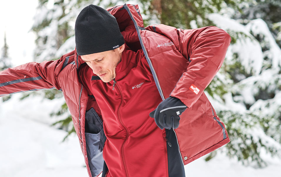A man putting on a Columbia Outdry coat in a snowy forest.