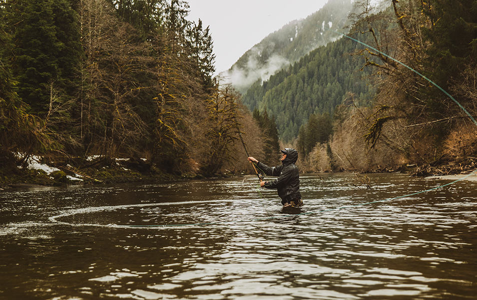 Pro angler Curtis Ciszek stands in the river casting a fly rod on a cold, rainy day.
