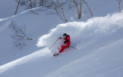 Alex Ferreira skis down a gorgeous powder bowl as a giant spray of snow envelops his entire body as light reflects around him. 
