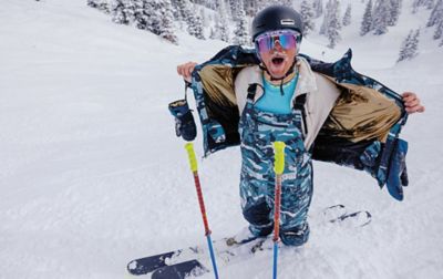 A skier with snow caked in his mustache removes his ski coat as he stands on a powdery ski run. 