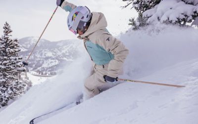A skier comes down a scenic ski run with trees in the background as she navigates deep powder. 