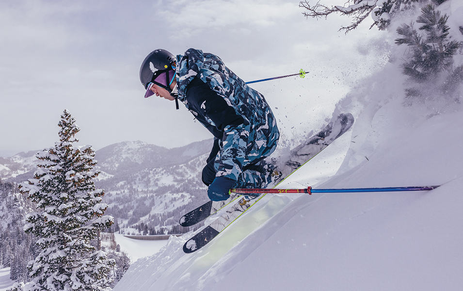 A skier catches air as he rips down a powder-filled ski run in a retro-style Columbia Sportswear ski suit. 