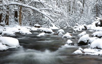 Snow-covered boulders line a flowing river as it rushes through a winter landscape in Great Smoky Mountains National Park.