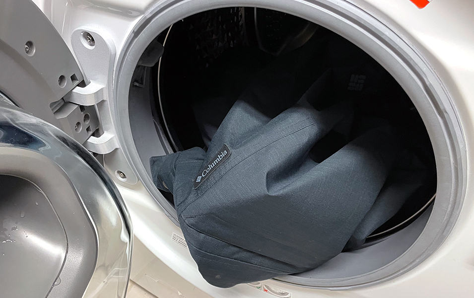 A ski jacket is pictured in a dryer with the door open.  