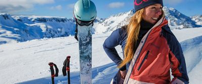 A skier takes off her jacket on a beautiful sunny day on the mountain. 