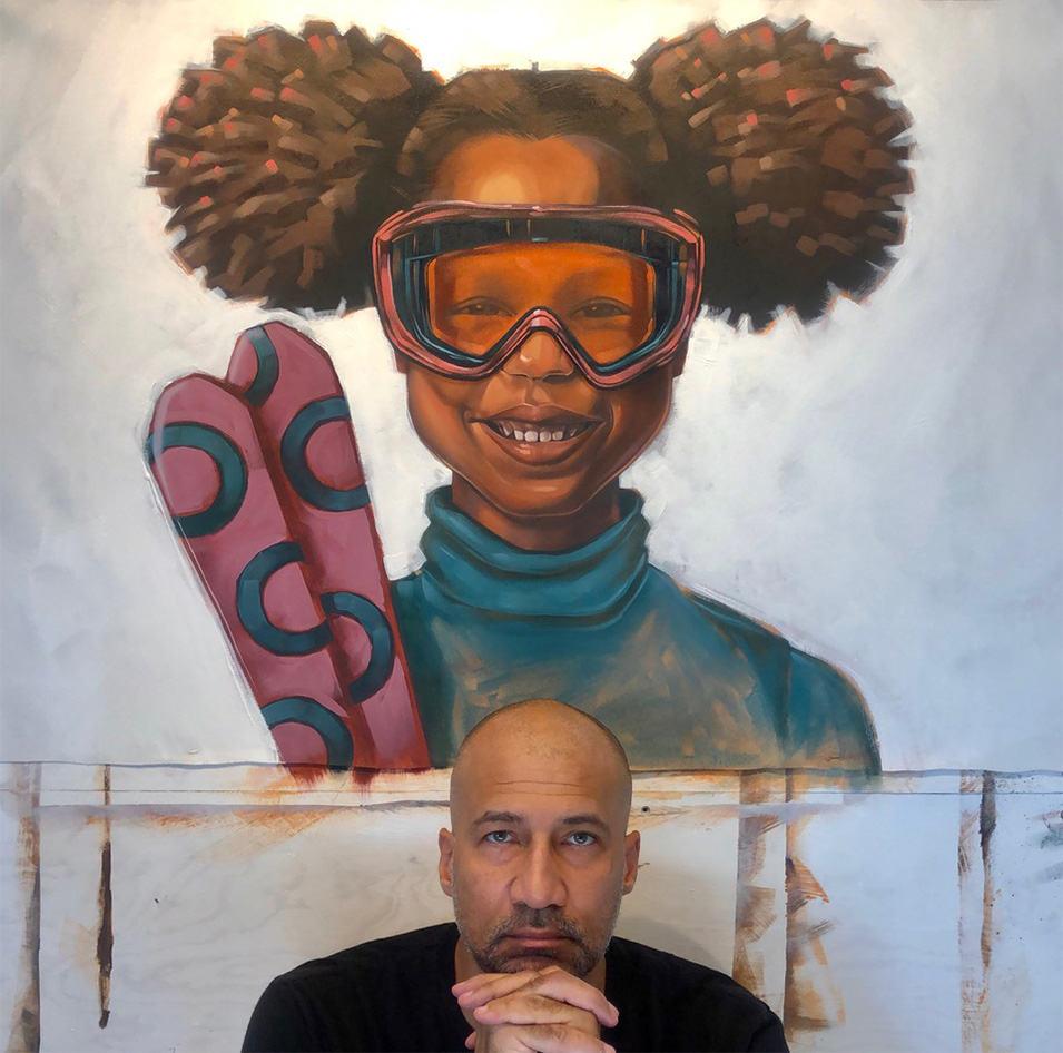Lamont Joseph White sits in front of one of his paintings staring at the camera.  