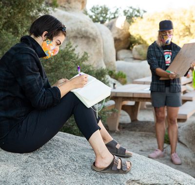 Mid course, Ada jots down notes in her notebook while sitting on a rock.