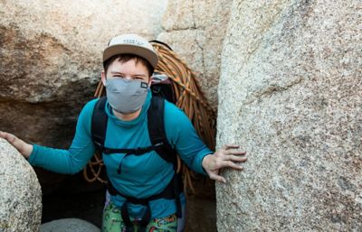 Mari between two boulders, smiling at the camera under her mask.