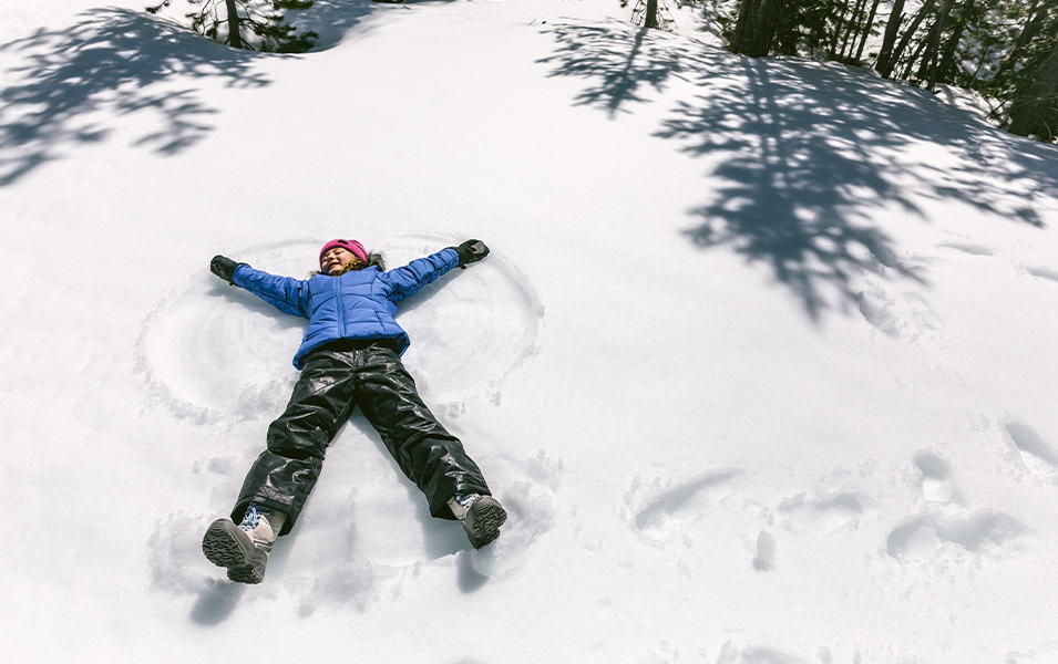 A girl making snow angels in a snowy landscape.