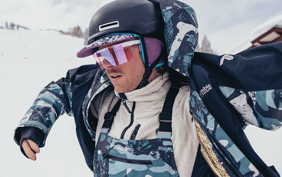 A skier takes off his blue Columbia Sportswear jacket, exposing his winter layers. 