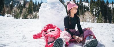 A girl sits in the snow with a red puffer jacket to her side. 