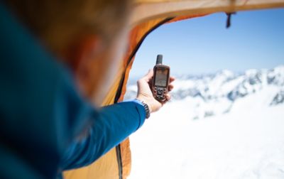 A man holds a GPS navigation device out of the window of a tent in a snowy setting. 

 
