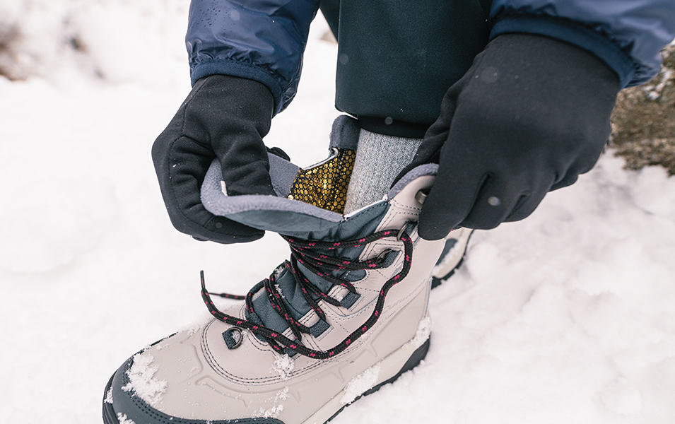A winter camper ties his hiking boots in the snow. 

 