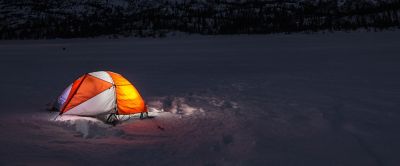 A tent is pictured in a beautiful winter setting at night. 