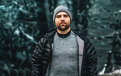 A man wearing an unzipped black Columbia Sportswear jacket with a gray baselayer shirt underneath it stares at the camera with a serious face. 