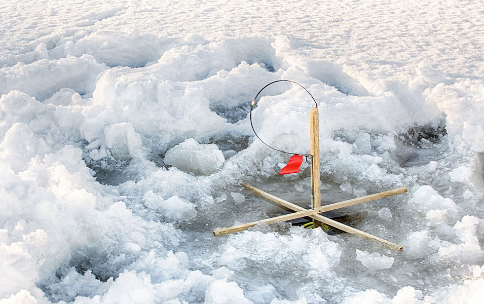 A tip-up trap with a red flag sites above an ice hole with slush and snow all around it. 