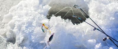 A close-up image of the end of a fishing rod hovering over an ice hole. 