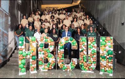 A group of staff and volunteers from Greening Youth Foundation stand in front of a sign filled with balloons that says “HBCUI.”
