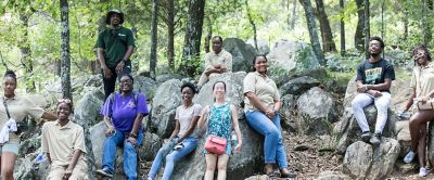 A group of staff and volunteers from Greening Youth Foundation sits in a pretty forest smiling at the camera. 