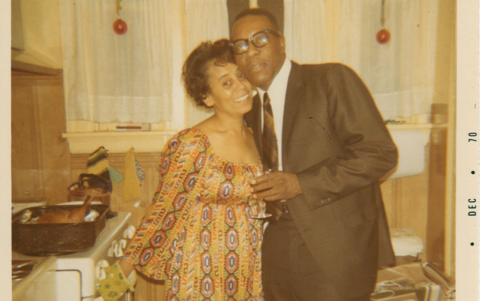 An old snapshot timestamped “Dec 1970” shows Benjamin and Frances Graham standing in the kitchen smiling at the camera. 