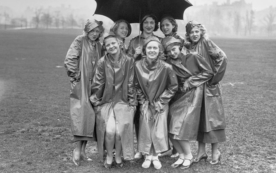 Members of the Chester Hale Troupe of Dancing Girls huddle under an umbrella wearing thick rain slickers in 1933.