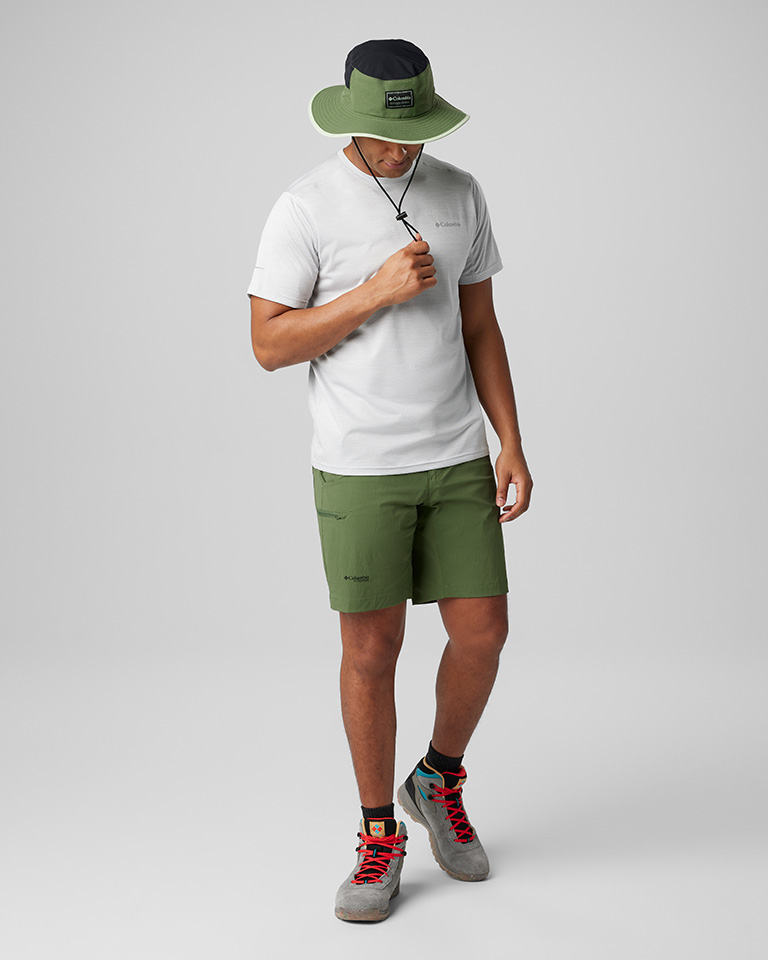 A man in a green wide-brimmed hat, white tee, and green shorts with hiking boots.