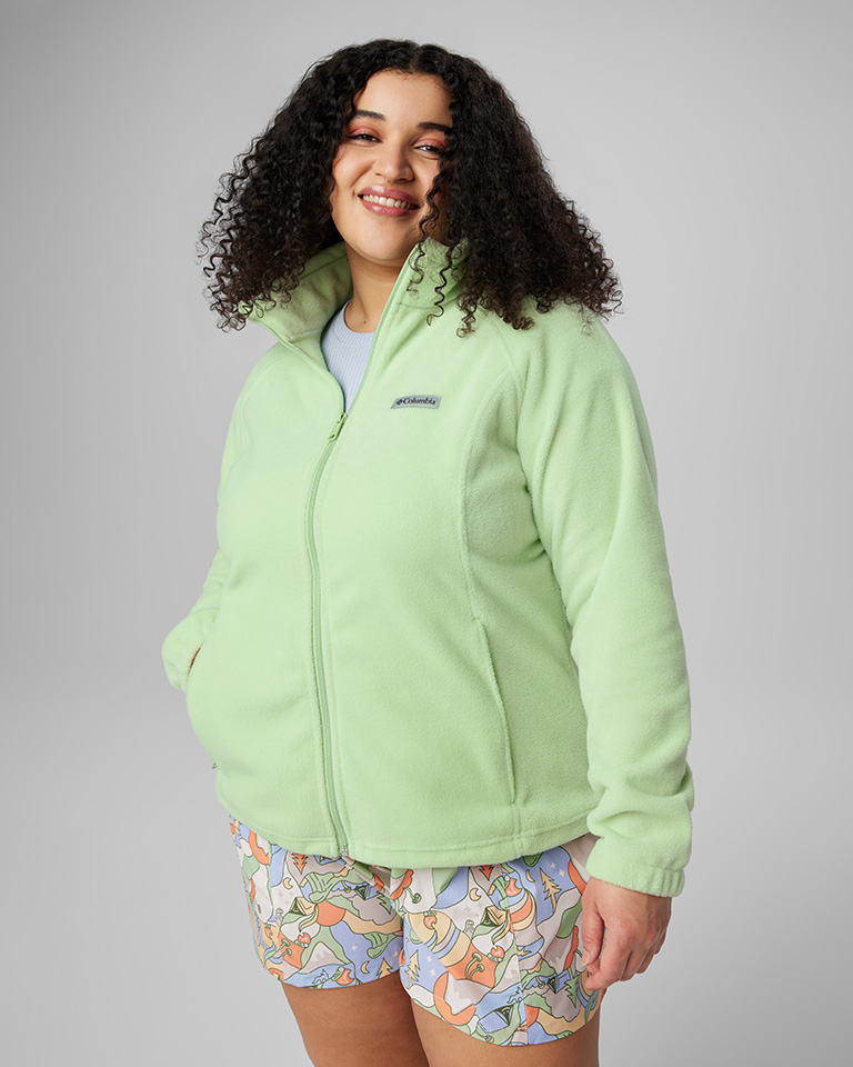 A woman in a mint green fleece zipped up over a light-colored tee with a colorful patterned short.