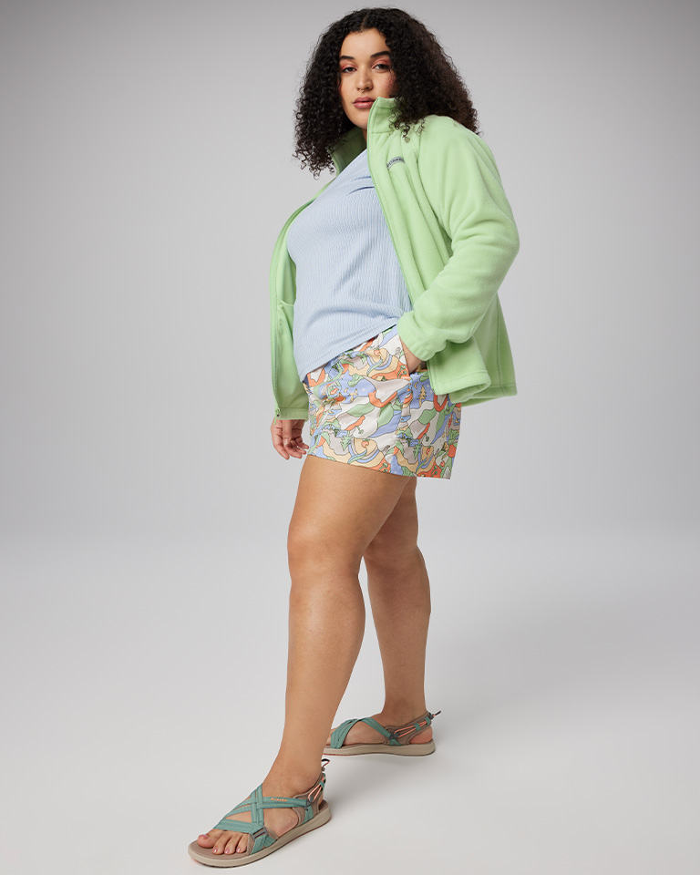 A woman wearing a green fleece, multi-colored skirt and blue sandals.