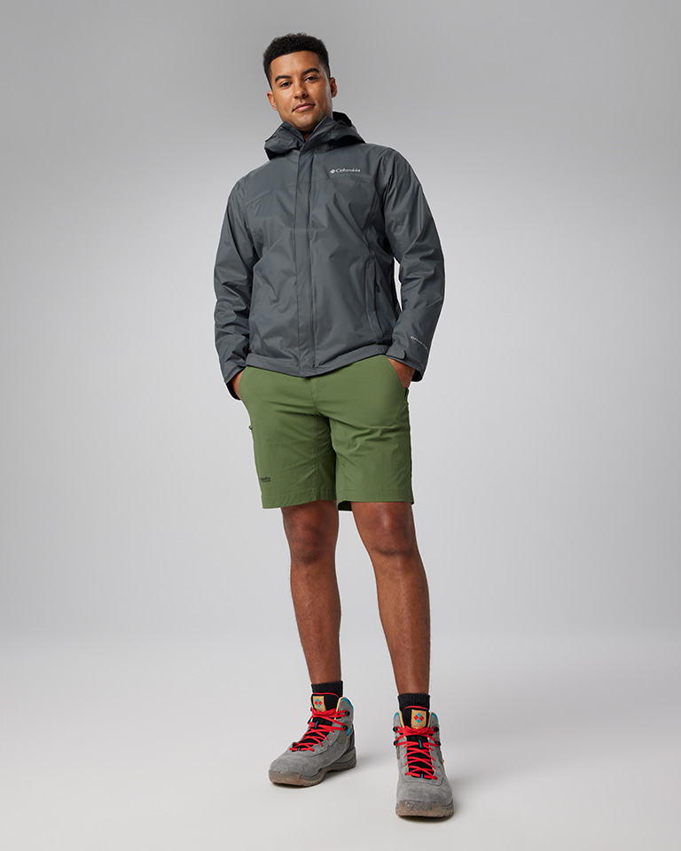 A man in a dark gray zippered jacket, green shorts, and hiking boots.