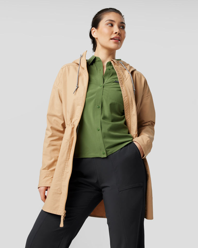 A woman in a green button-down shirt and tan jacket.