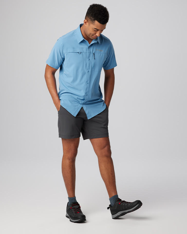 A man in a blue button-down shirt, shorts, and hiking shoes.
