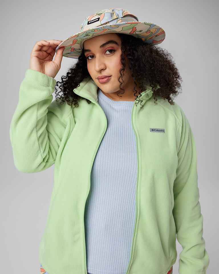 A woman in a colorful bucket hat, light blue shirt, and light green fleece.