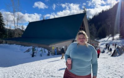 Snoqualmie ski patroller Annet Soot stands near a ski lodge holding a pink thermos and wearing a blue Columbia Sportswear baselayer top.