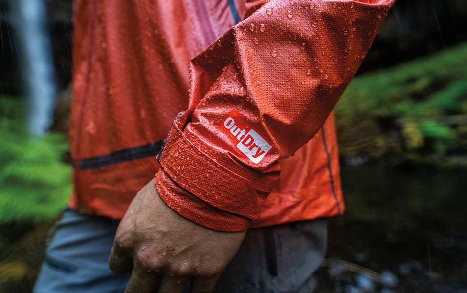 A close-up shot of the lower arm and waist of a man wearing a red Columbia Sportswear rain jacket with the OutDry logo on his wrist.
