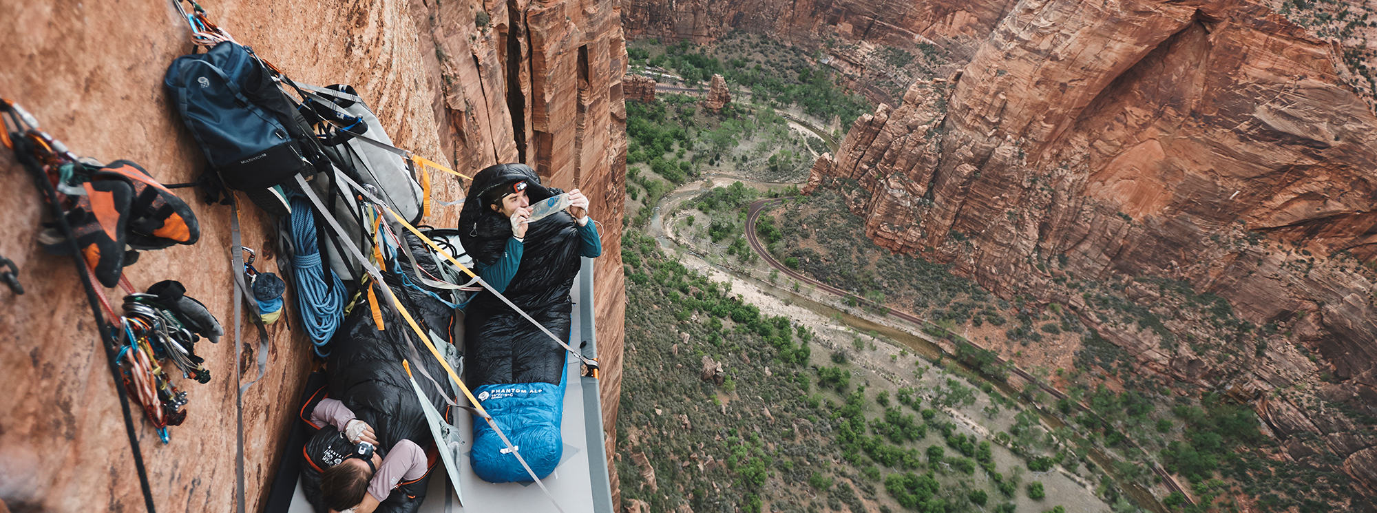 On a portal ledge in Zion National Park, Ethan and his climbing partner take in the views from their sleeping bags at dawn