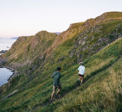 Two trail runners running on a hillside trail in Norway in clear serene weather.
