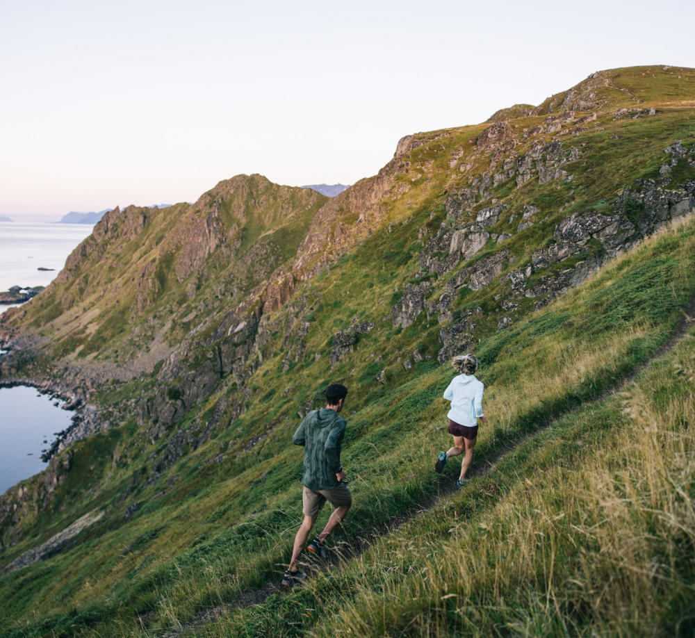 Two trail runners running on a hillside trail in Norway in clear serene weather.