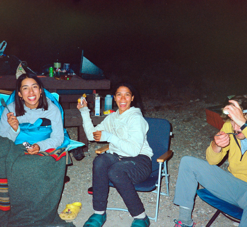 Three campers around the campfire smile.