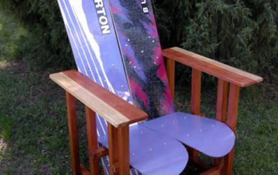 An adirondack chair made from recycled snowboards sits on a grassy lawn.