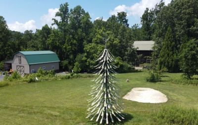 A tall tree made from skis stands on a beautiful piece of property featuring a scenic barn in the background. 