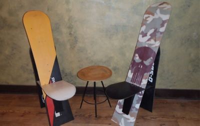 Two high-back seats made from recycled snowboards sit next to a small coffee table on a wood floor. 