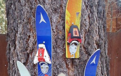 A collection of cool wall-mounted bottle openers made from old skis hang from a tree on display. 