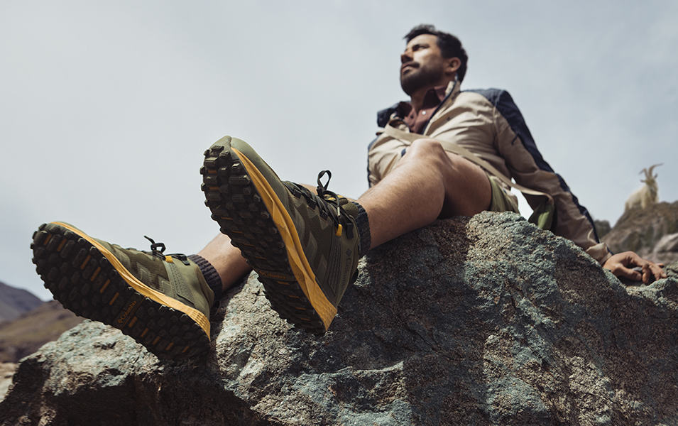 A hiker sits on a rock dangling his Columbia Sportswear Facet 75 Mid shoes over the edge. 