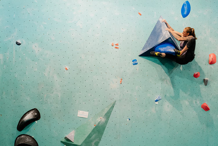 Alex Johnson bouldering on a teal wall in a gym.