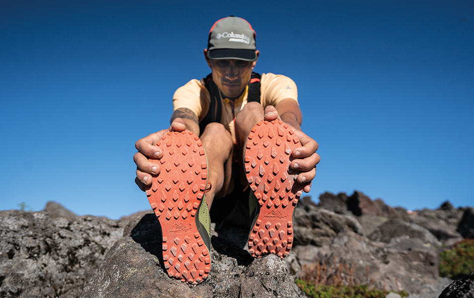 Columbia Sportswear athlete Yassine Diboun sits on a rocky trail stretching and touching his toes.